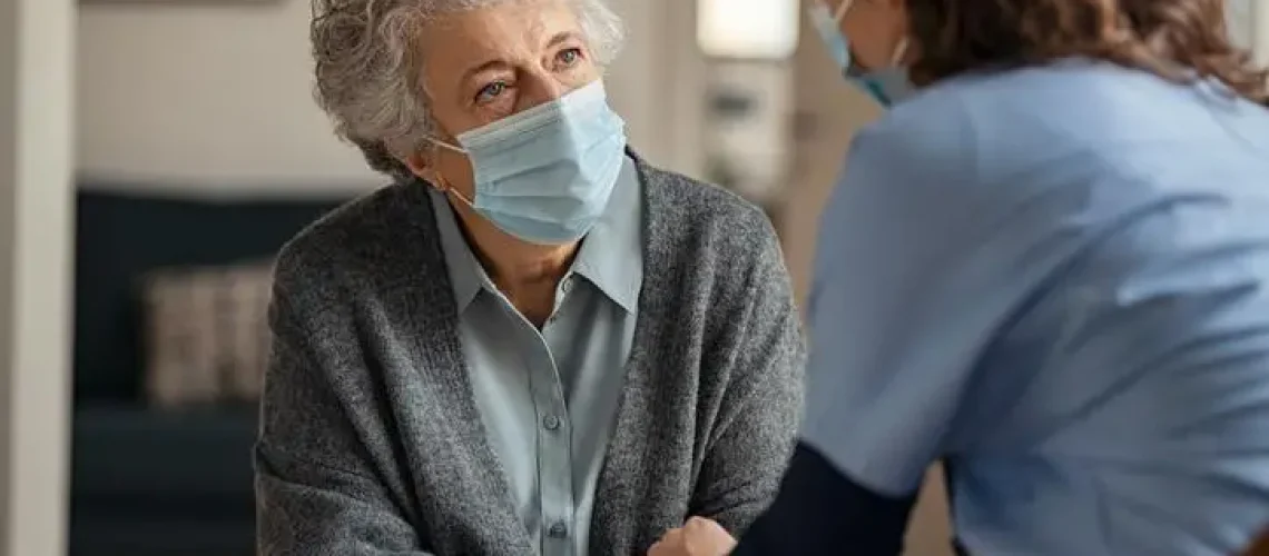 Female doctor consoling senior woman wearing face mask during home visit